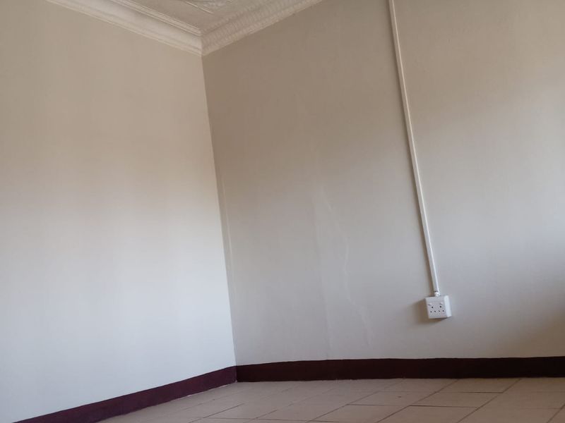 An empty bedroom featuring tiled flooring, ornate ceiling molding, and visible wall cracks with surface-mounted electrical wiring.