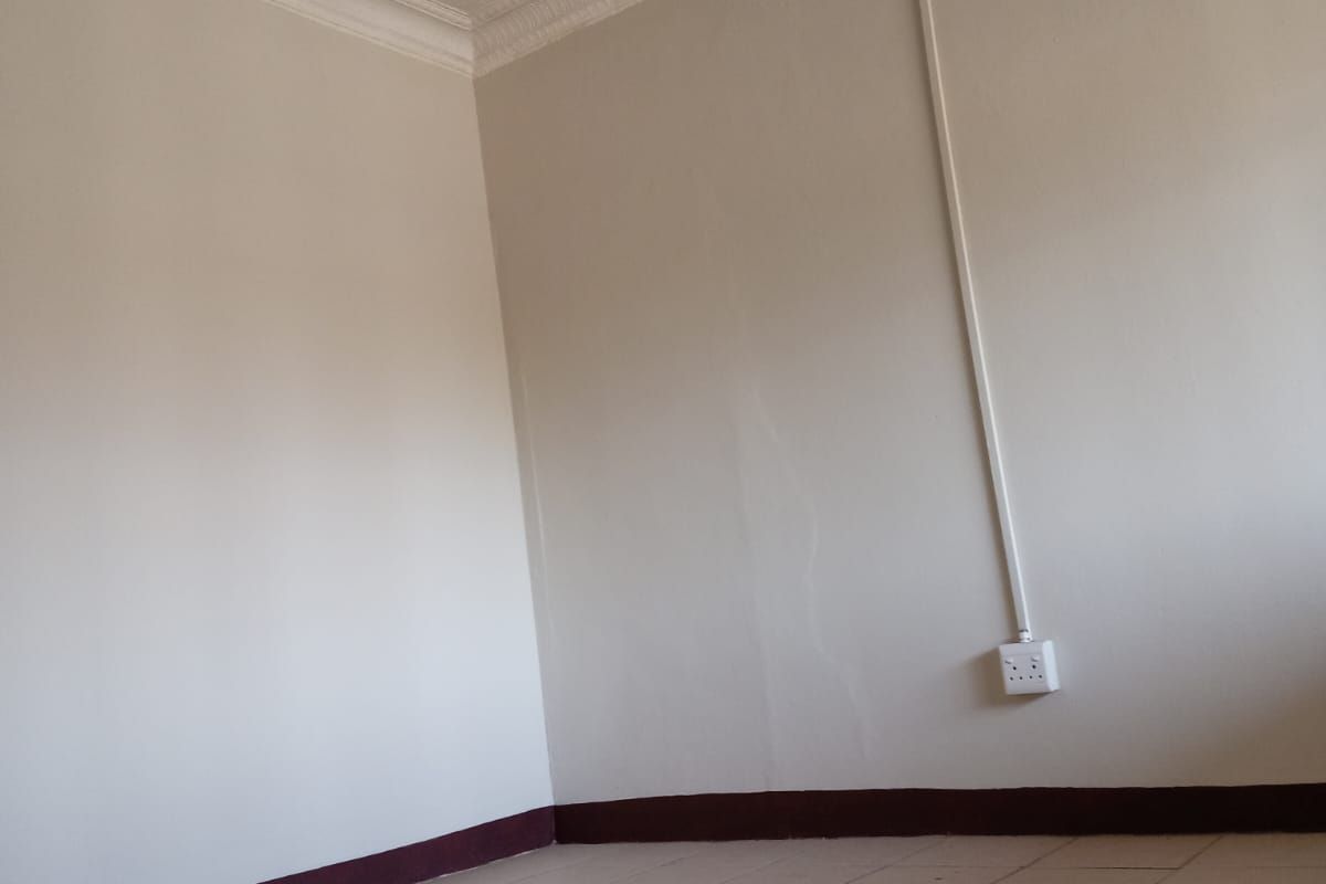 An empty bedroom featuring tiled flooring, ornate ceiling molding, and visible wall cracks with surface-mounted electrical wiring.