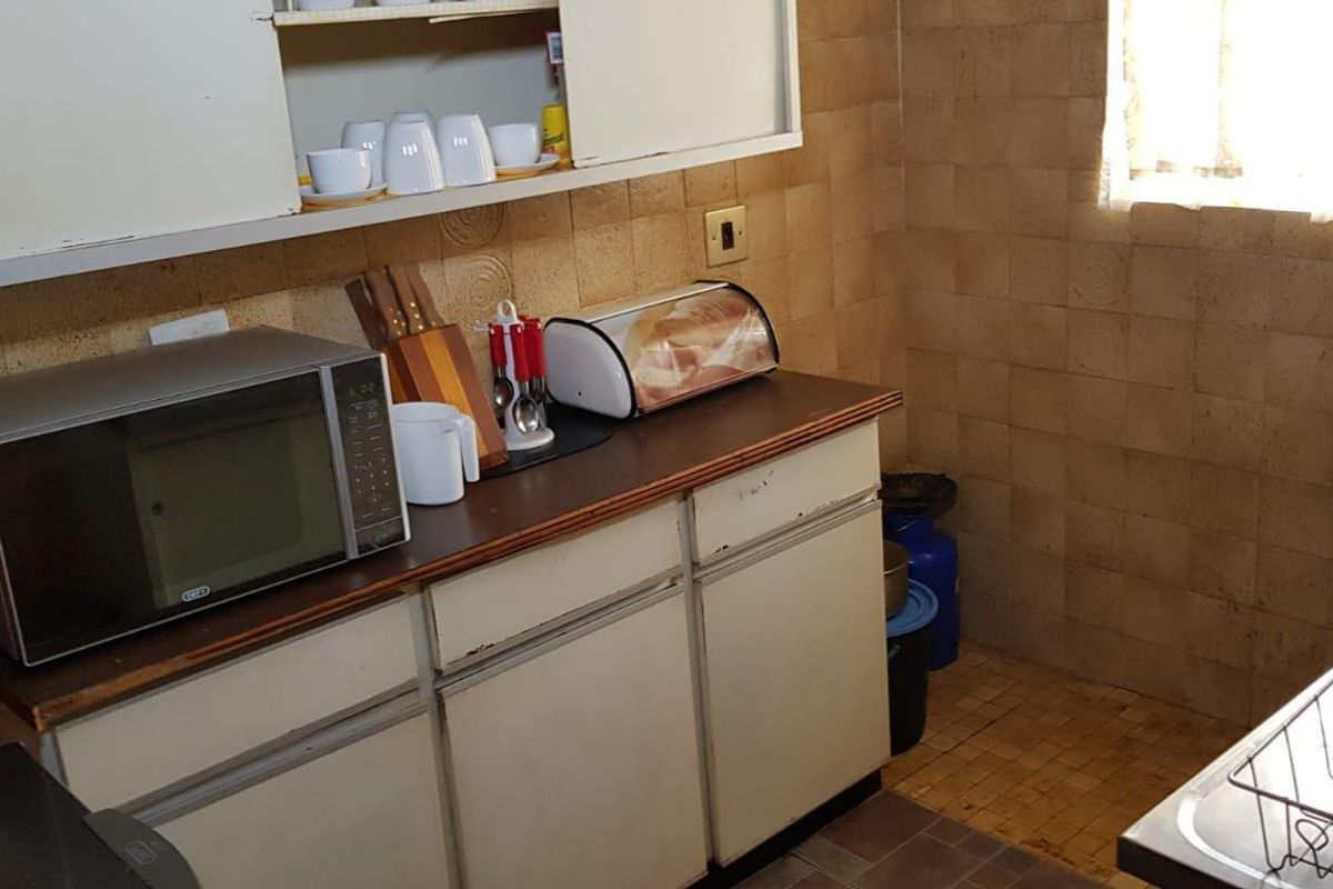 A dated kitchen featuring original cabinetry, tiled wall splashbacks, and tiled flooring, offering significant potential for a modern renovation.