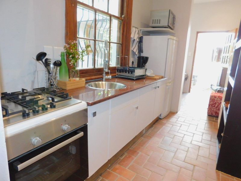 A functional kitchen featuring a gas stove, oven, granite countertops, stainless steel sink, and traditional terracotta floor tiles.