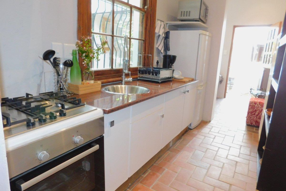 A functional kitchen featuring a gas stove, oven, granite countertops, stainless steel sink, and traditional terracotta floor tiles.
