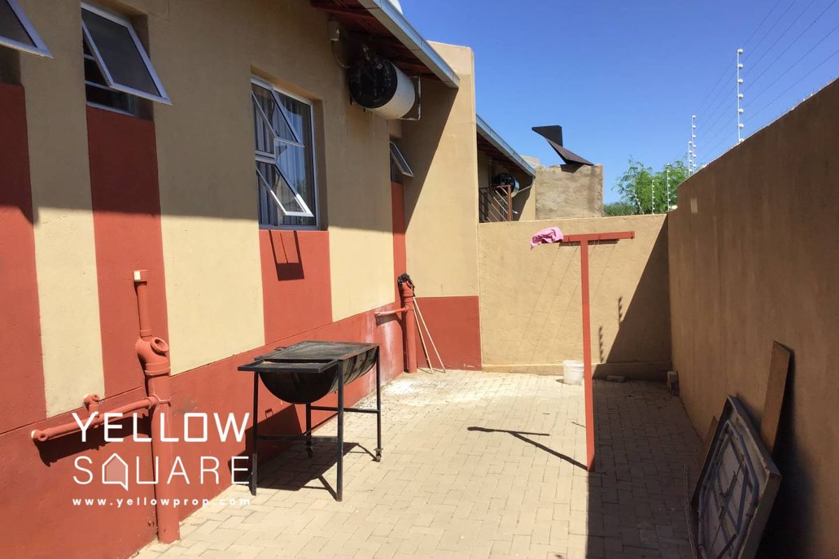 A paved rear courtyard area featuring an exterior wall-mounted geyser and perimeter boundary walls.