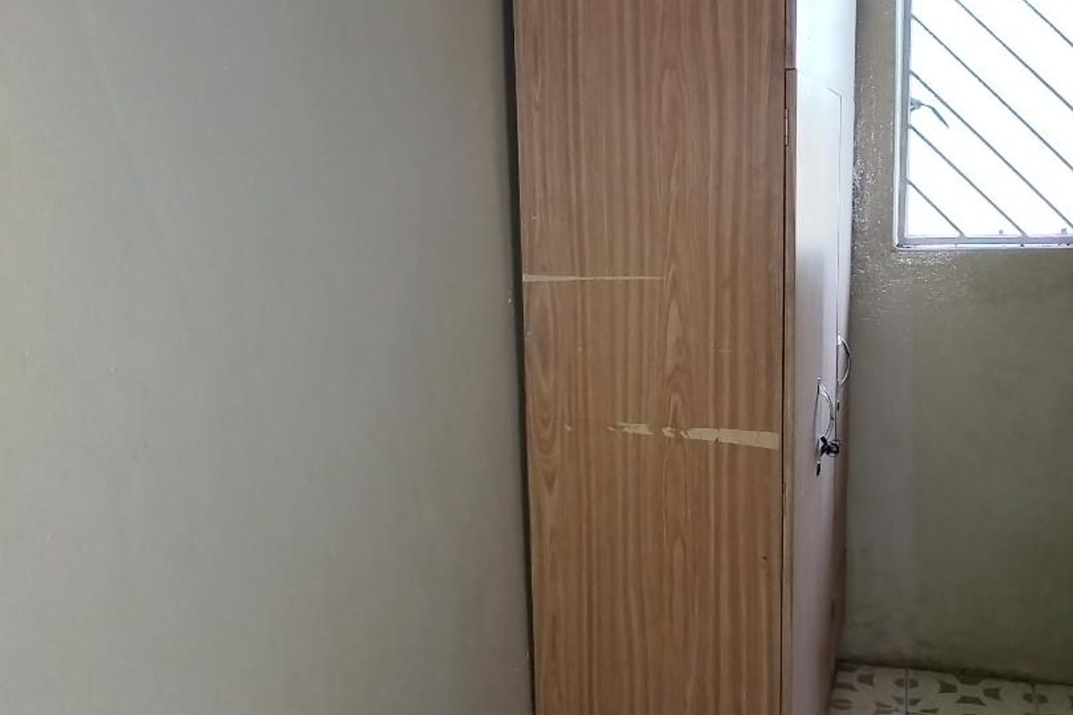 A small bedroom featuring tiled flooring, a window with security bars, and visible wall damage requiring maintenance and cosmetic updates.