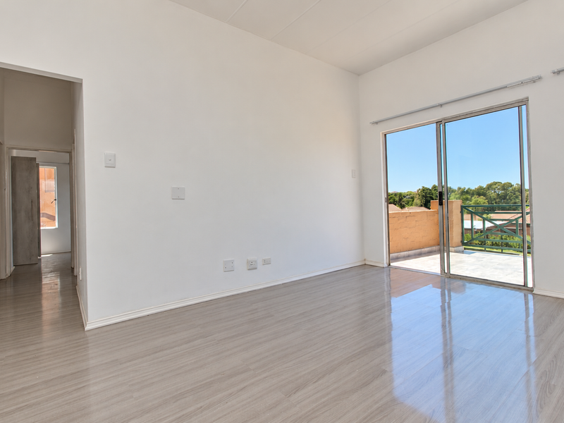 Bright and spacious living area featuring modern laminate flooring, neutral walls, and direct access to a private balcony through large sliding glass doors.