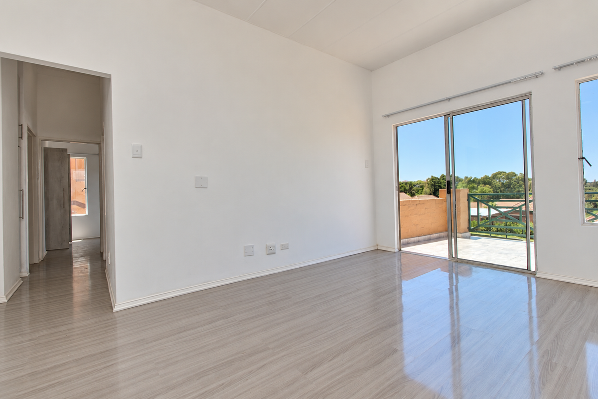 Bright and spacious living area featuring modern laminate flooring, neutral walls, and direct access to a private balcony through large sliding glass doors.