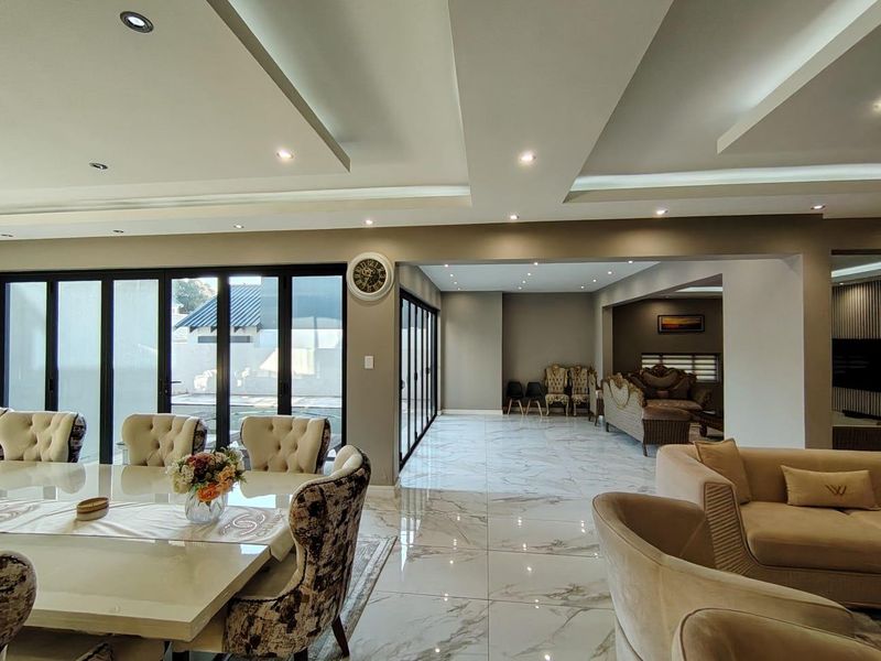 Spacious open-plan living and dining area featuring modern coffered ceilings, recessed lighting, and polished marble-look floor tiles with large sliding doors to the exterior.