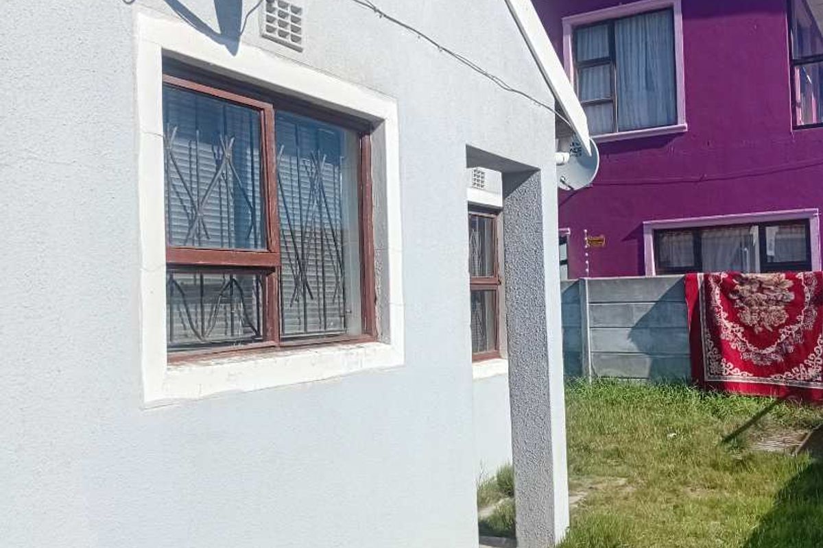 Rear exterior view of the property showing the side facade, satellite dish, and a small garden area with a boundary wall.