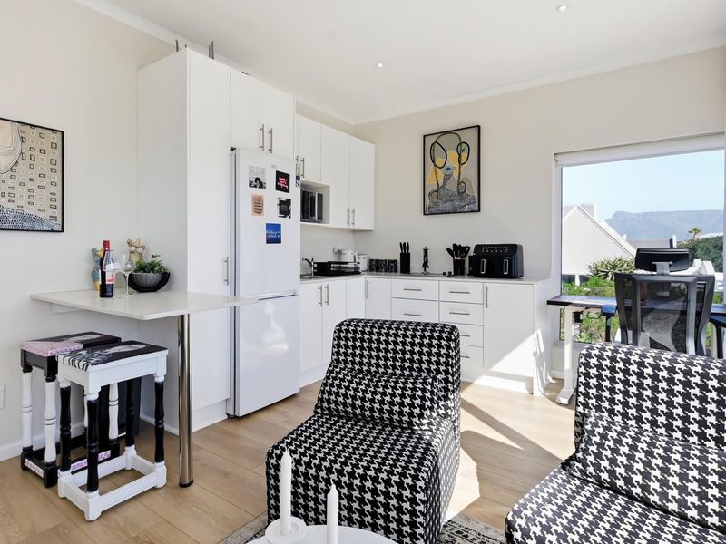 Bright open-plan living area featuring modern white cabinetry, laminate flooring, and a large window with natural light.