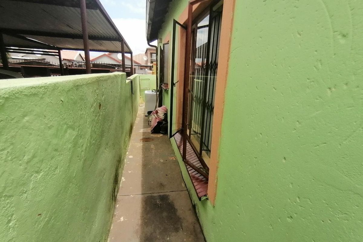 A narrow side passage of the house featuring a concrete walkway, boundary wall, and security gate access to the main structure.