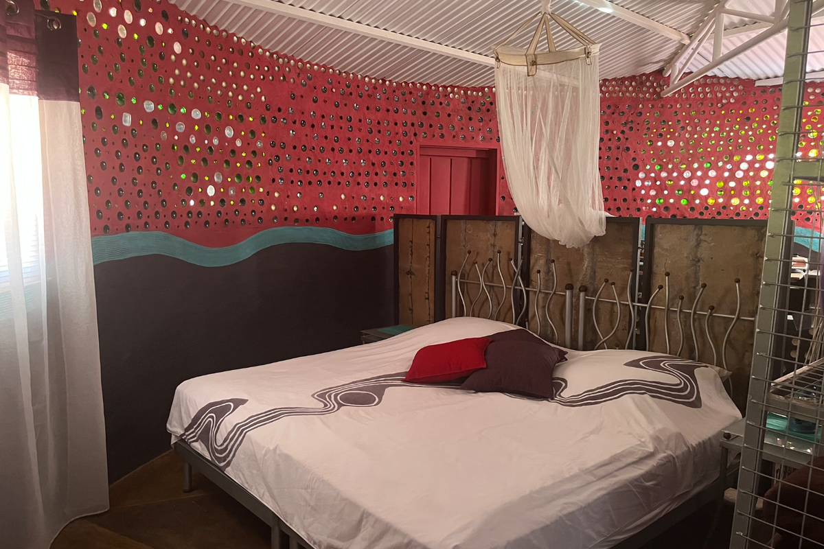 A unique bedroom featuring distinctive bottle-embedded wall construction, exposed corrugated metal roofing, and a rustic aesthetic.