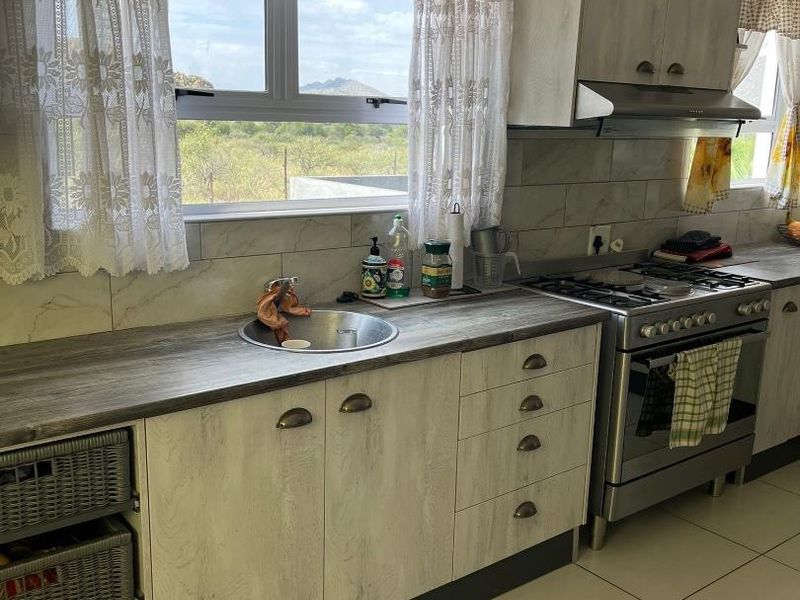 A functional kitchen featuring light wood-grain cabinetry, stainless steel gas stove with extractor, tiled backsplash, and a stainless steel sink overlooking the landscape.