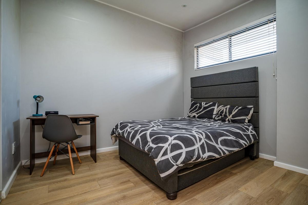 A well-maintained bedroom featuring light wood-look flooring, neutral grey walls, and a high-set horizontal window with fitted blinds.