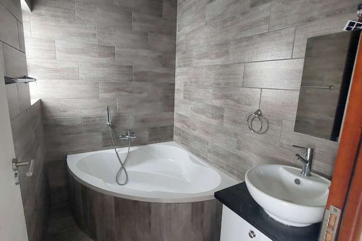 Modern bathroom featuring a corner bathtub, vessel sink with vanity cabinet, and contemporary wood-look wall and floor tiling.
