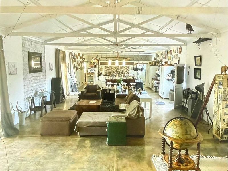 Spacious open-plan living and kitchen area featuring high exposed roof trusses, polished concrete floors, and a rustic exposed brick feature wall.