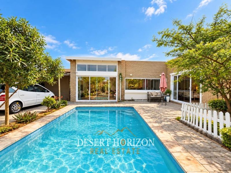 A well-maintained outdoor pool area featuring a paved patio, brick exterior facade, and large sliding glass doors providing access to the home.
