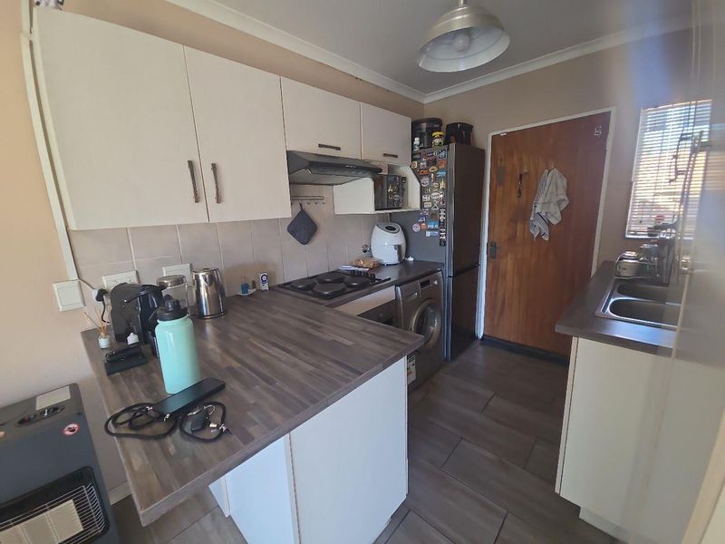 A functional kitchen featuring laminate countertops, built-in cabinetry, an electric hob with extractor fan, and tiled flooring.