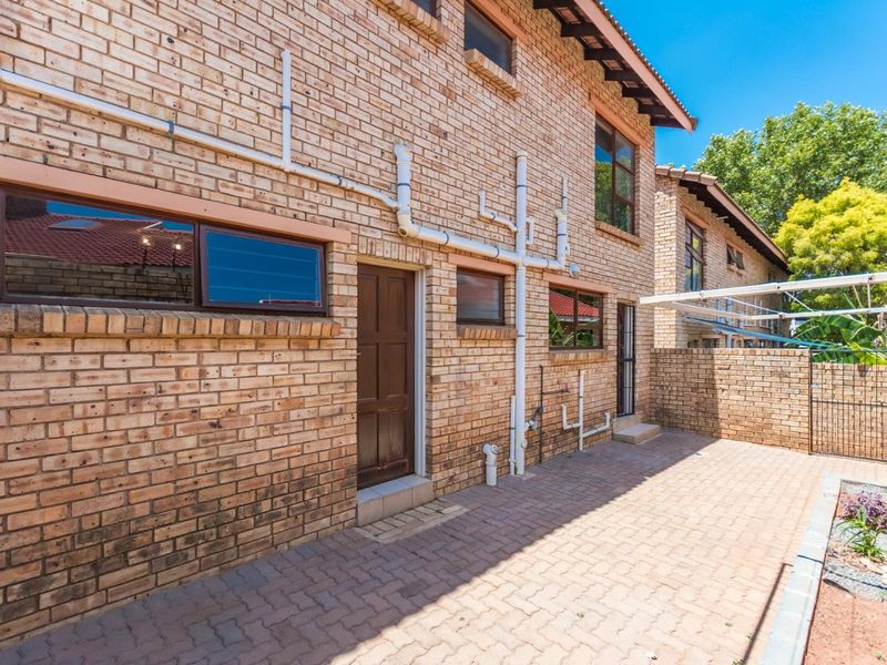 Rear exterior view of the townhouse featuring a paved courtyard, face brick facade, and external plumbing infrastructure.
