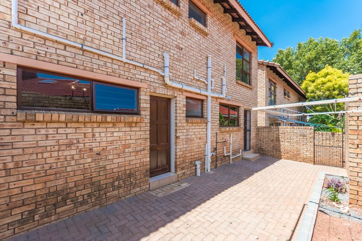 Rear exterior view of the townhouse featuring a paved courtyard, face brick facade, and external plumbing infrastructure.