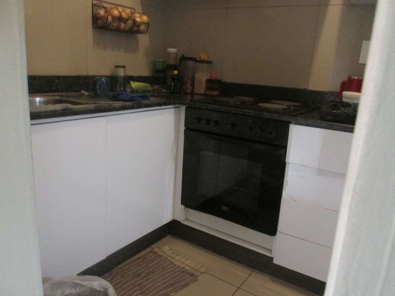 Compact kitchen featuring white cabinetry, granite countertops, a built-in oven, and an electric hob with tiled backsplash and flooring.