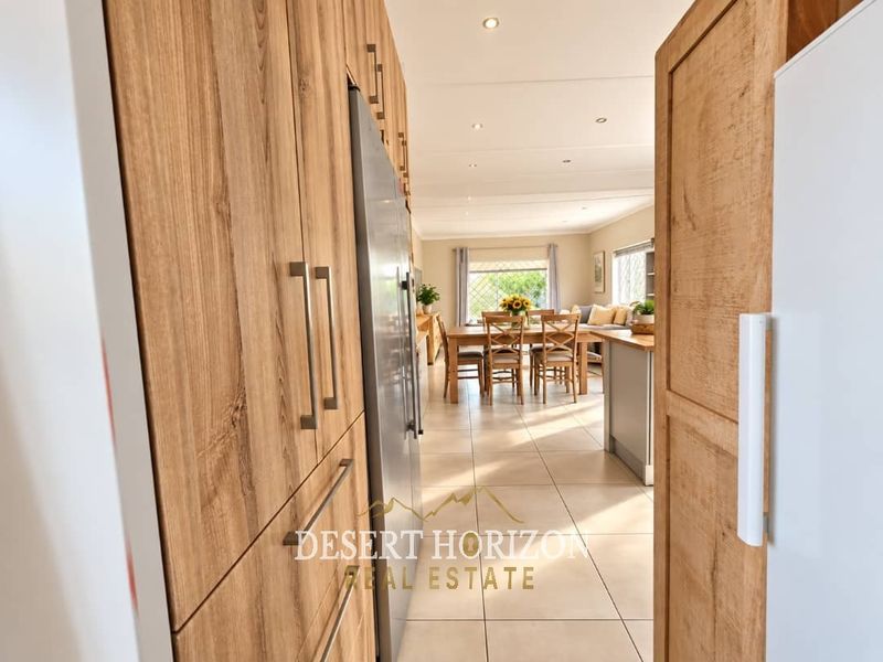 An open-plan living and dining area featuring modern wood-look cabinetry, tiled flooring, and recessed lighting, creating a bright and cohesive living space.