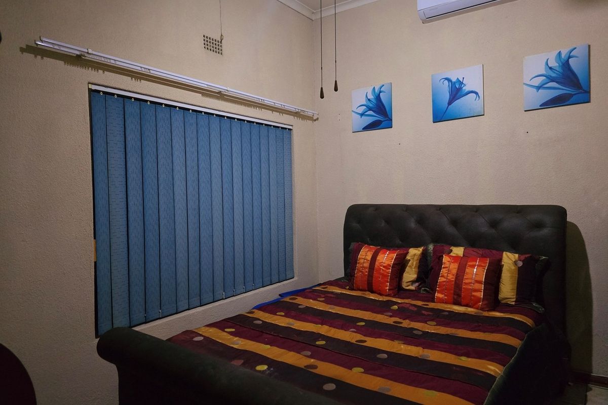 A bedroom featuring vertical blinds and a wall-mounted air conditioning unit.