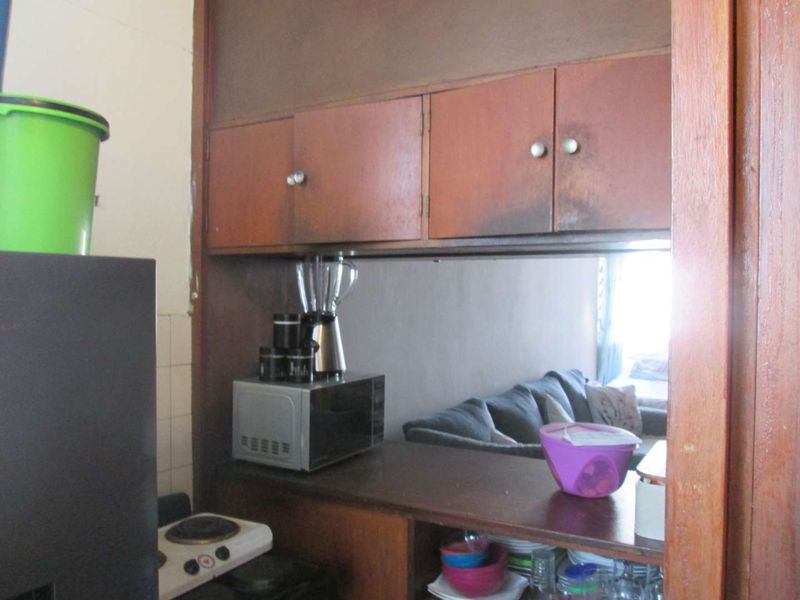 A compact kitchen area featuring dated built-in cabinetry and a serving hatch opening into the adjacent living space.
