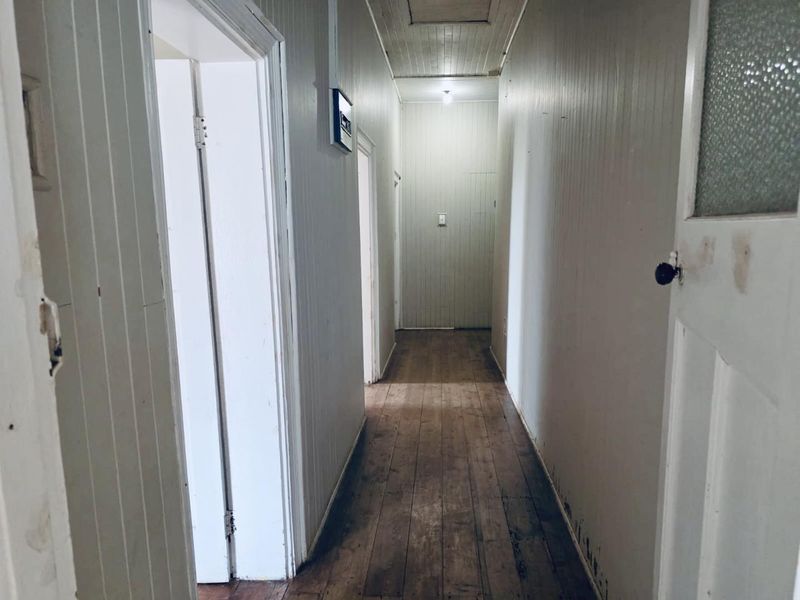 A long, empty hallway featuring original timber floorboards and vertical timber wall paneling, providing access to multiple rooms.