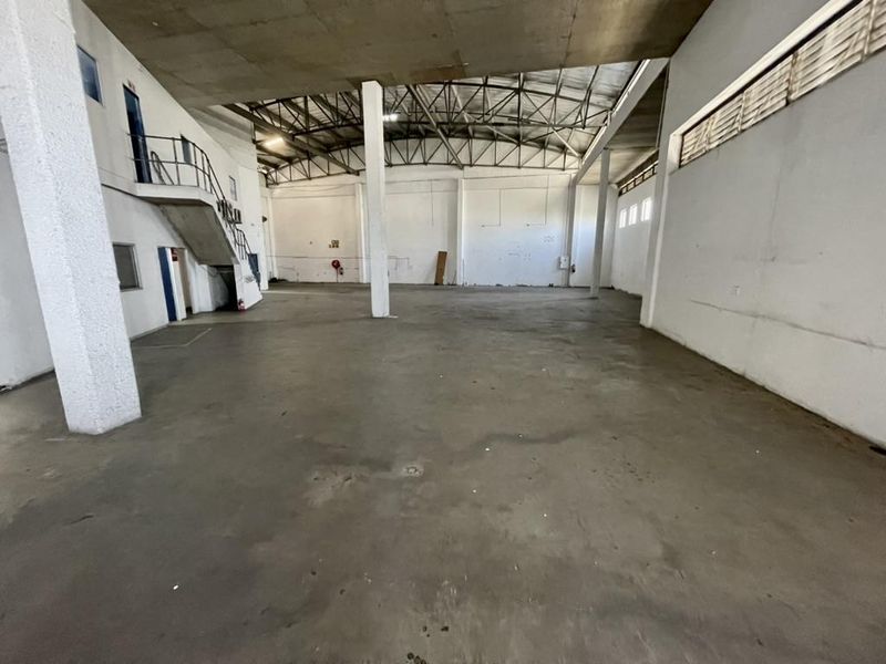 Spacious industrial warehouse area featuring high ceilings, exposed steel trusses, concrete flooring, and an integrated mezzanine staircase.
