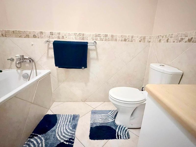 A functional bathroom featuring a bathtub, toilet, and vanity with neutral wall and floor tiling.