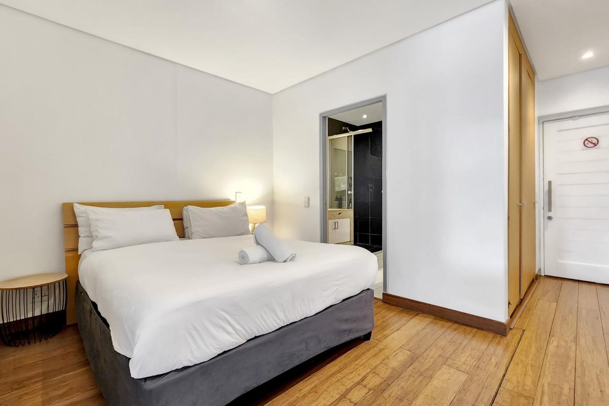 A well-maintained bedroom featuring warm hardwood flooring, built-in cupboards, and direct access to an en-suite bathroom.