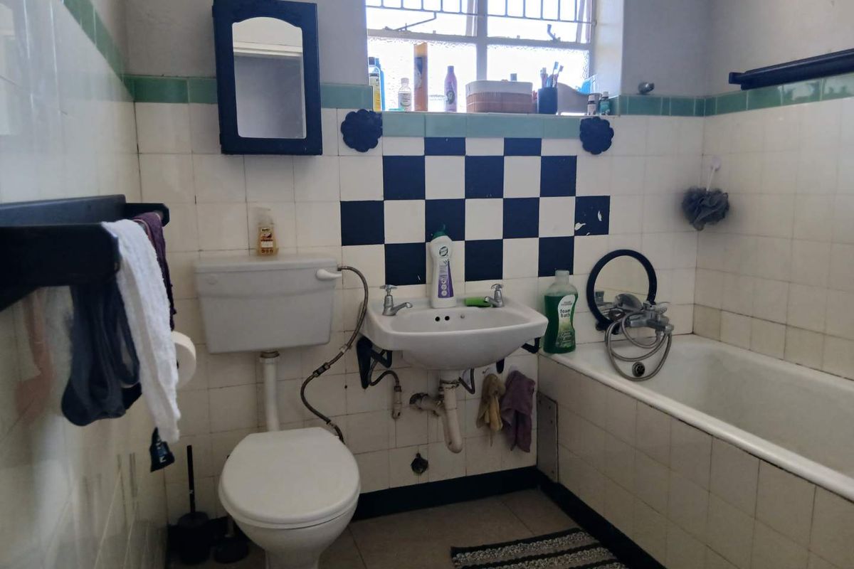 A dated bathroom featuring a standard bathtub, pedestal basin, and toilet, with original tiled walls and security bars on the window.