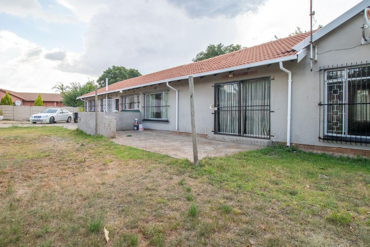 Rear view of the house featuring a concrete patio area, tiled roof, and security bars on windows and sliding doors.