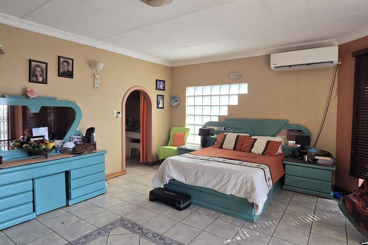 Spacious bedroom featuring tiled flooring, a wall-mounted air conditioning unit, glass block feature window, and an arched doorway leading to an adjoining space.