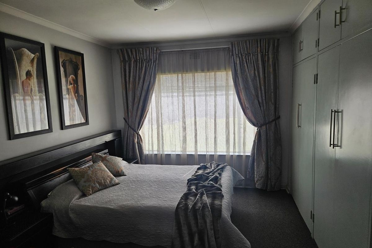 A well-maintained bedroom featuring built-in cupboards, carpeted flooring, and a large window with curtain treatments.