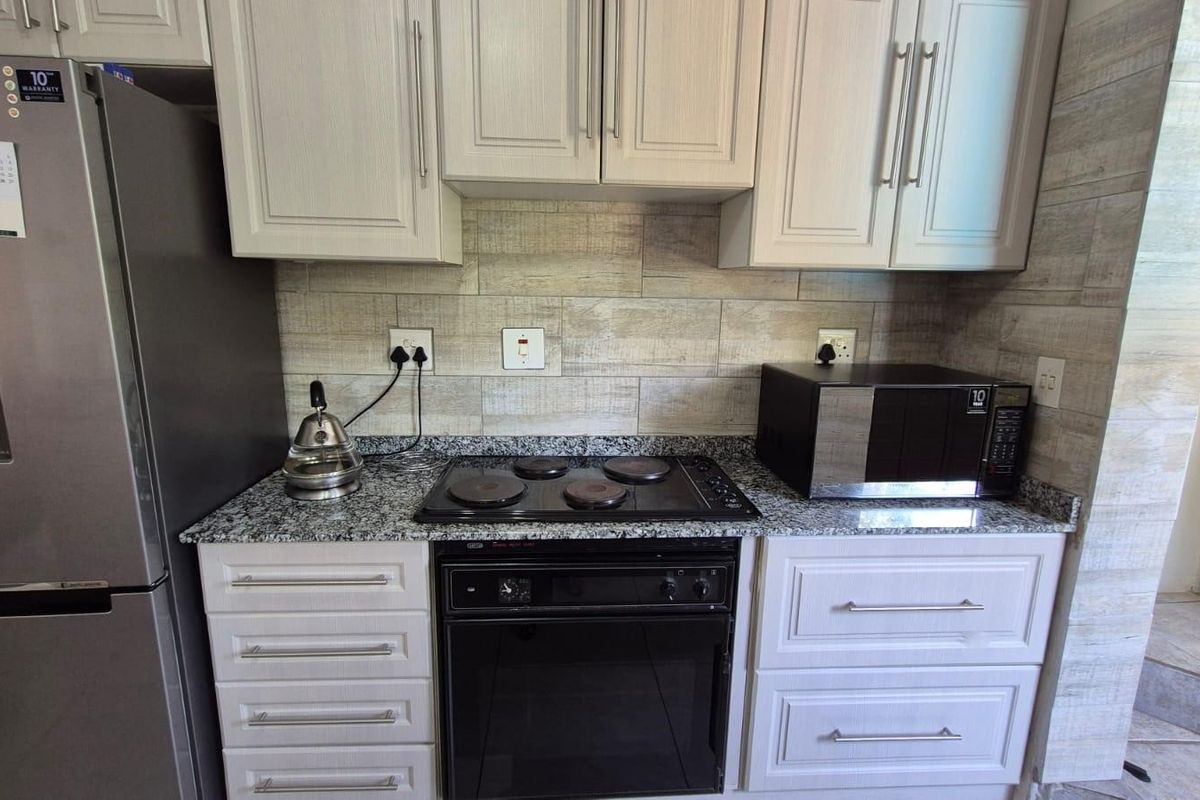 A well-maintained kitchen featuring light-toned cabinetry, granite countertops, a built-in electric oven and hob, and a modern tiled backsplash.