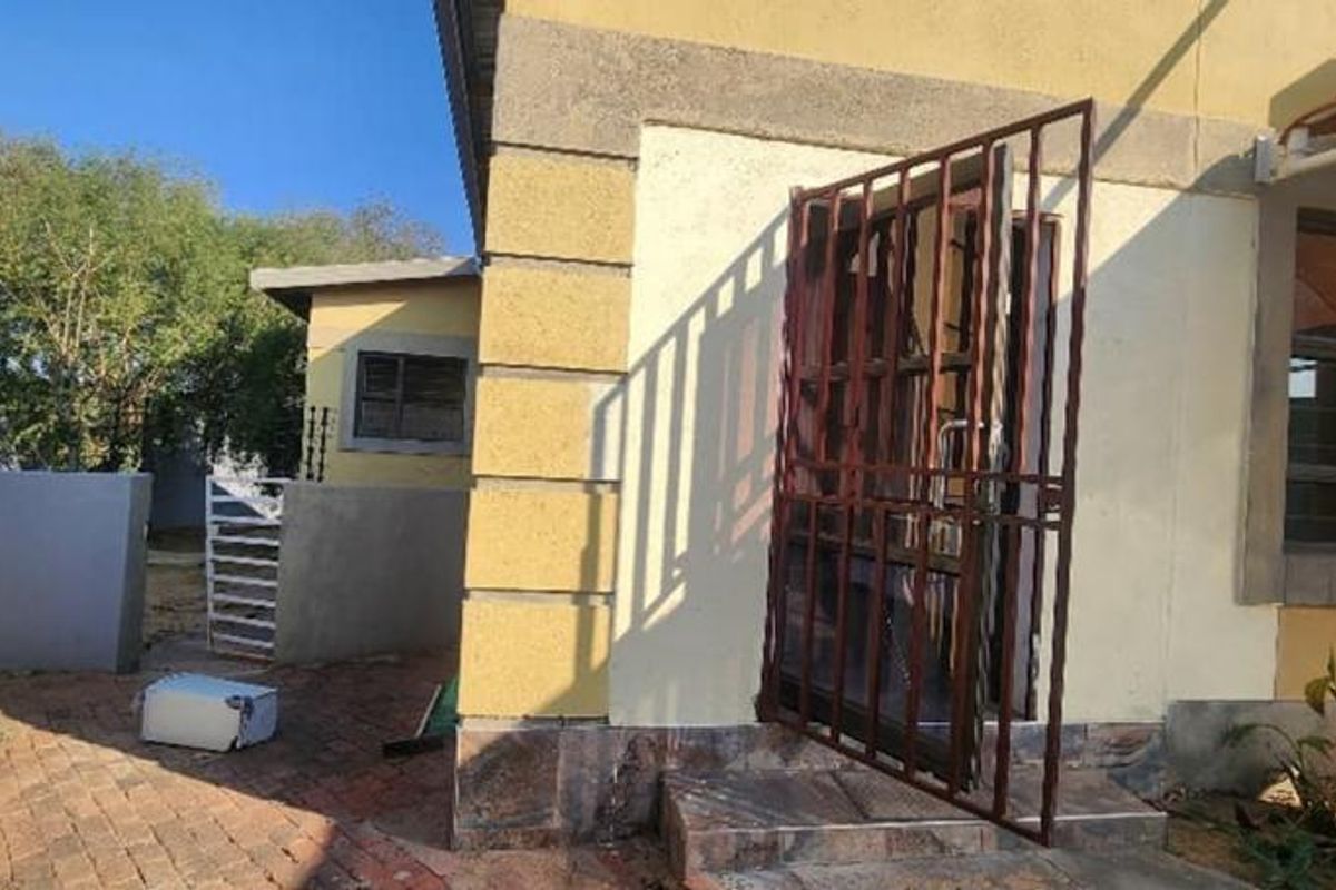 A view of the side exterior of the house featuring a paved walkway, security gate, and masonry wall finishes.