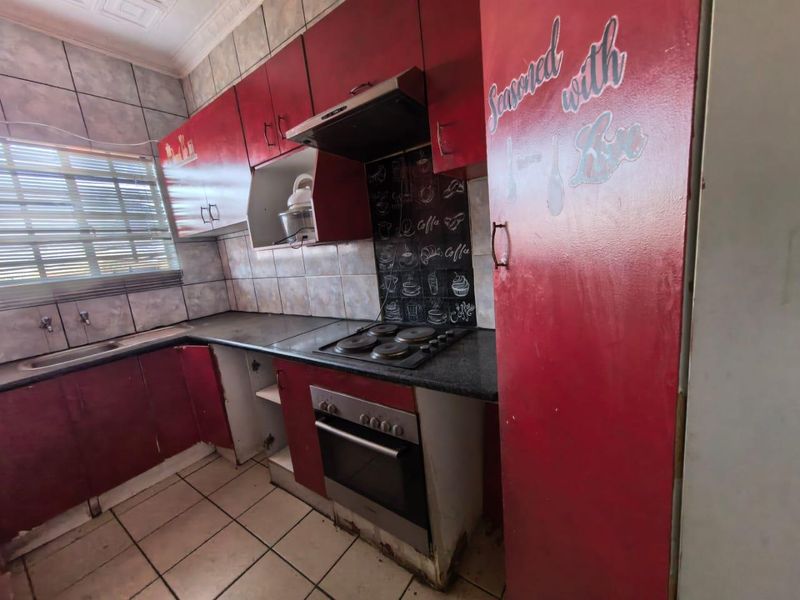 A dated kitchen featuring red cabinetry, built-in oven and hob, tiled splashbacks, and tiled flooring, requiring cosmetic updates to improve its overall condition.