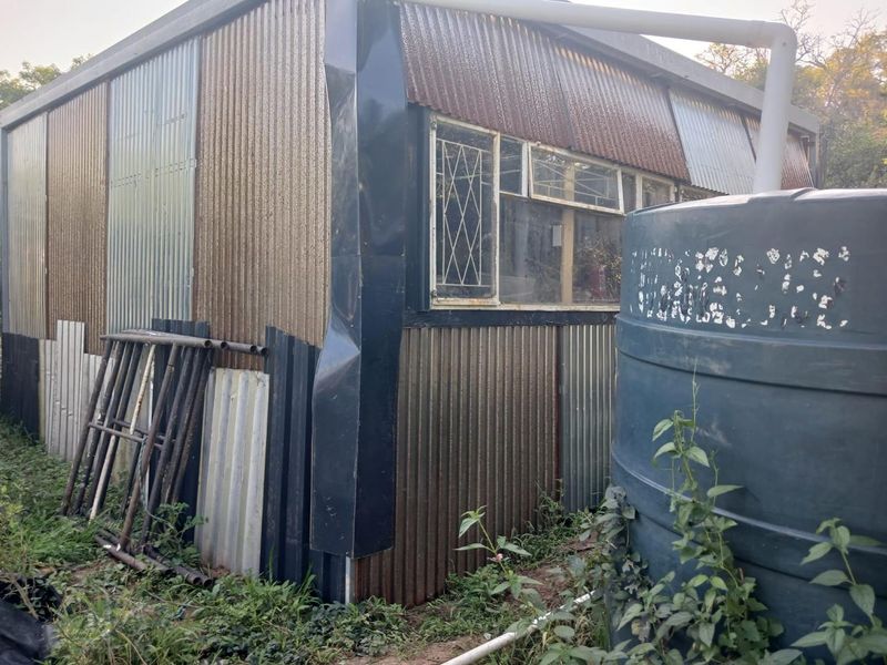 Rear view of a corrugated metal structure featuring security burglar bars and an external water storage tank.