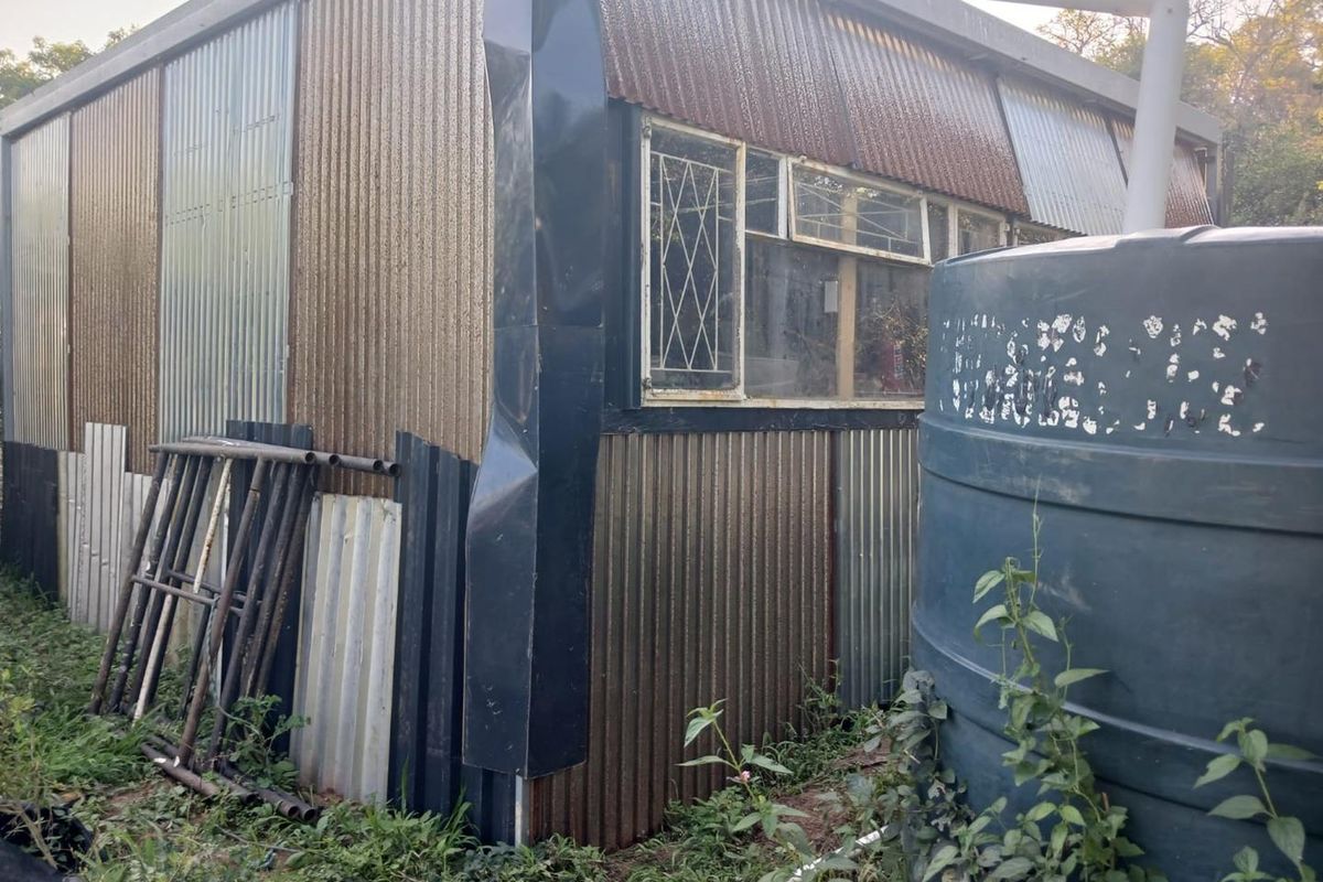 Rear view of a corrugated metal structure featuring security burglar bars and an external water storage tank.