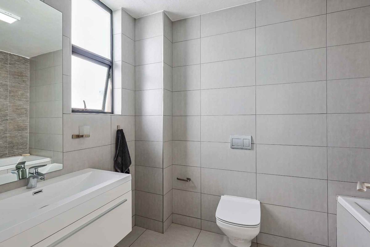 Modern bathroom featuring large format grey wall tiles, a wall-mounted vanity with integrated basin, and a concealed cistern toilet.