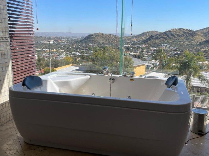 A modern bathroom featuring a large freestanding jetted bathtub positioned against floor-to-ceiling windows with expansive panoramic mountain and city views.