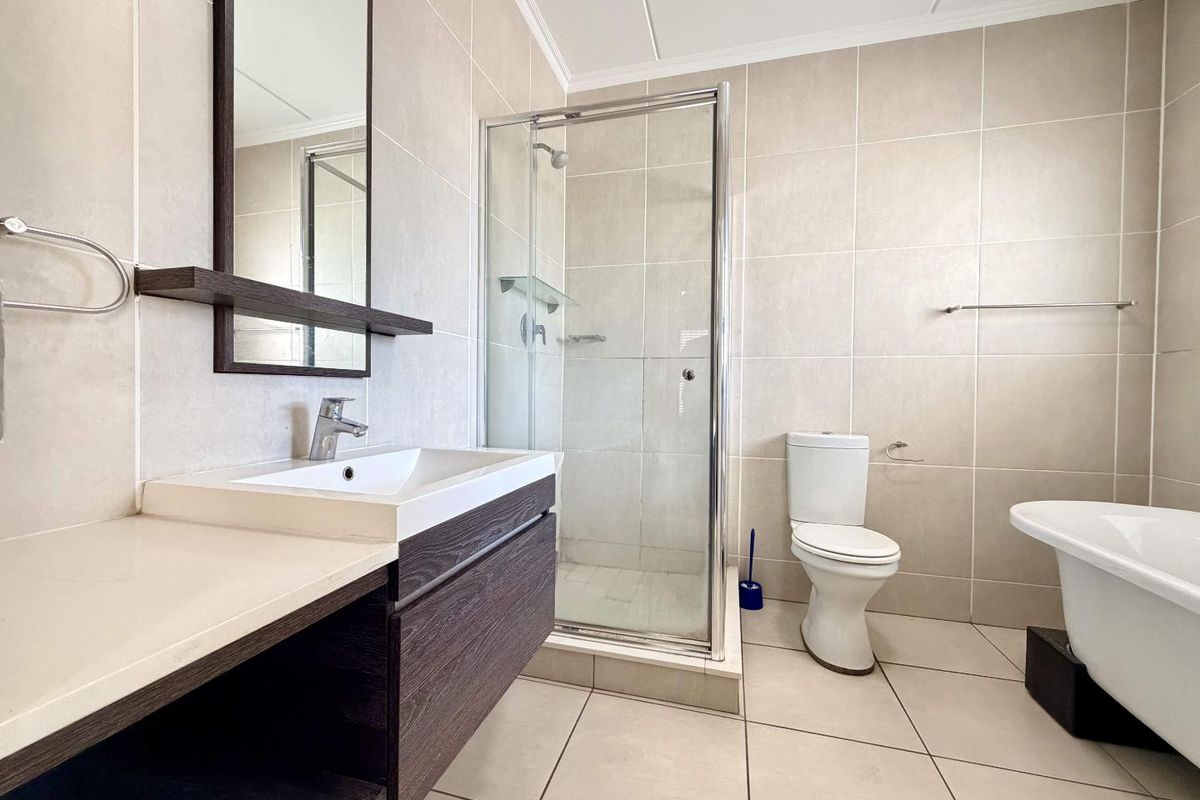Modern bathroom featuring a vanity with basin, glass-enclosed shower, toilet, and a freestanding bathtub with neutral wall and floor tiling.
