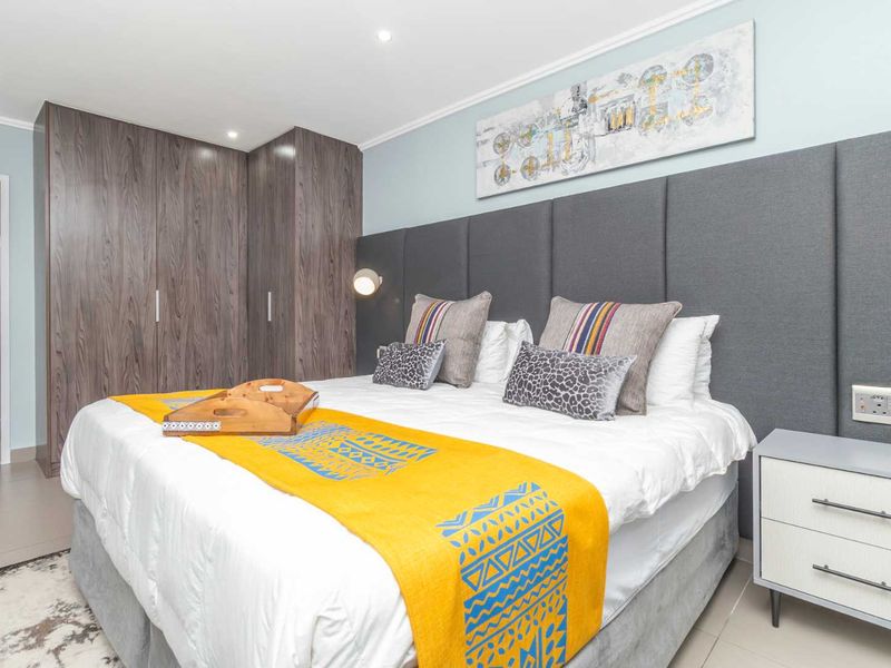 A well-maintained bedroom featuring built-in wooden cupboards, a large upholstered headboard, and modern recessed lighting.