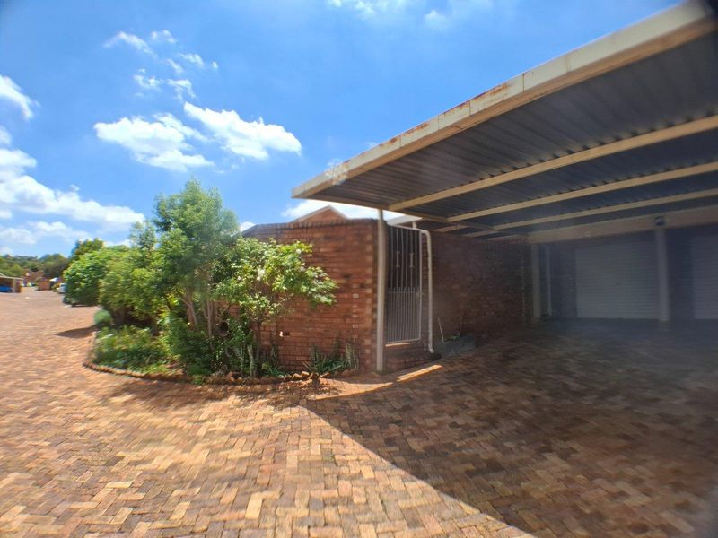 Front exterior view of the townhouse featuring a paved driveway, brick facade, and a covered carport area with a security gate entrance.