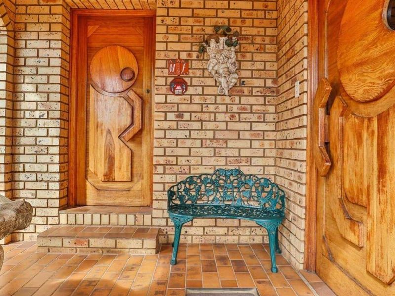 A covered entrance porch featuring exposed brick walls, terracotta-style tiled flooring, and distinctive custom-designed wooden doors.