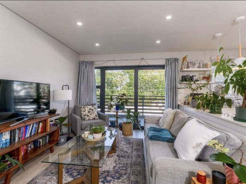 Bright open-plan living area featuring modern recessed lighting, laminate flooring, and seamless access to a private balcony through large sliding glass doors.