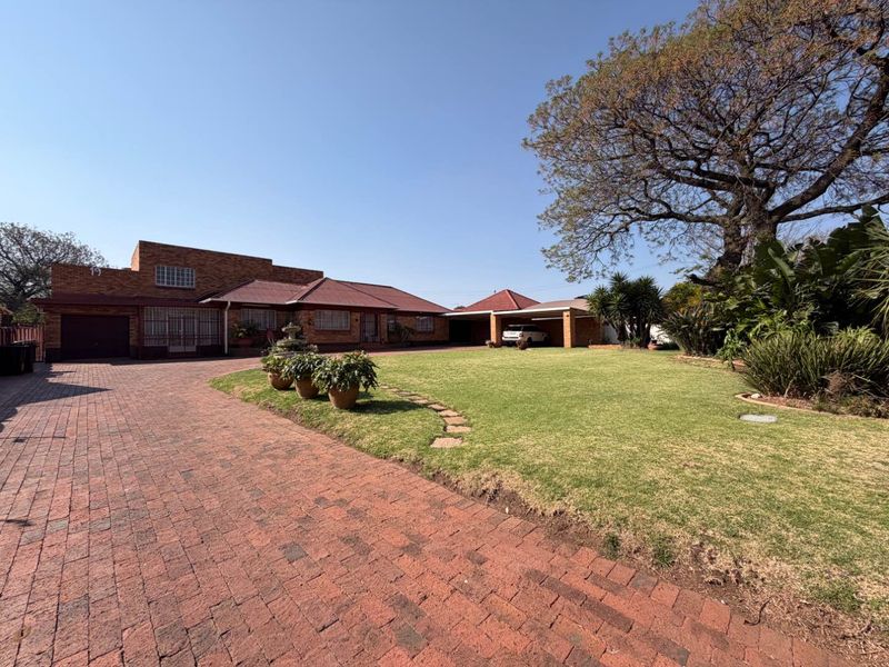 Spacious front exterior featuring a large brick driveway, well-maintained lawn, double carport, and a classic brick facade with secure gated access.