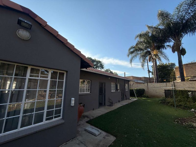 Rear view of the cottage featuring a lawn, concrete pathway, security gates, and a brick boundary wall.