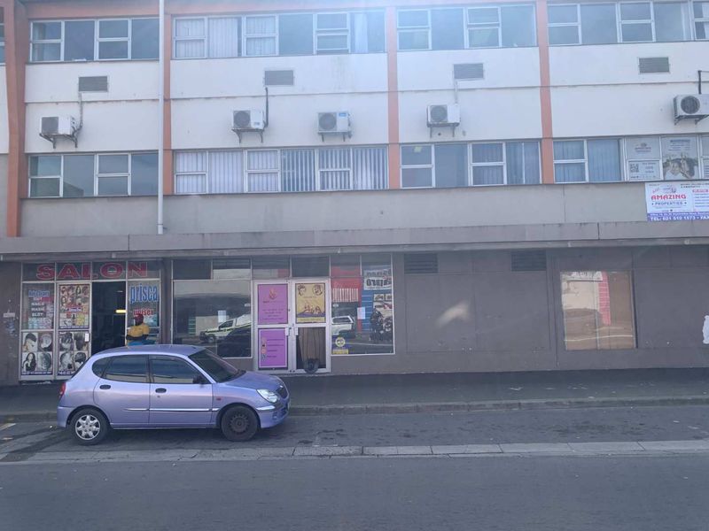 Street-level view of a multi-story commercial office building featuring ground-floor retail storefronts and wall-mounted air conditioning units.