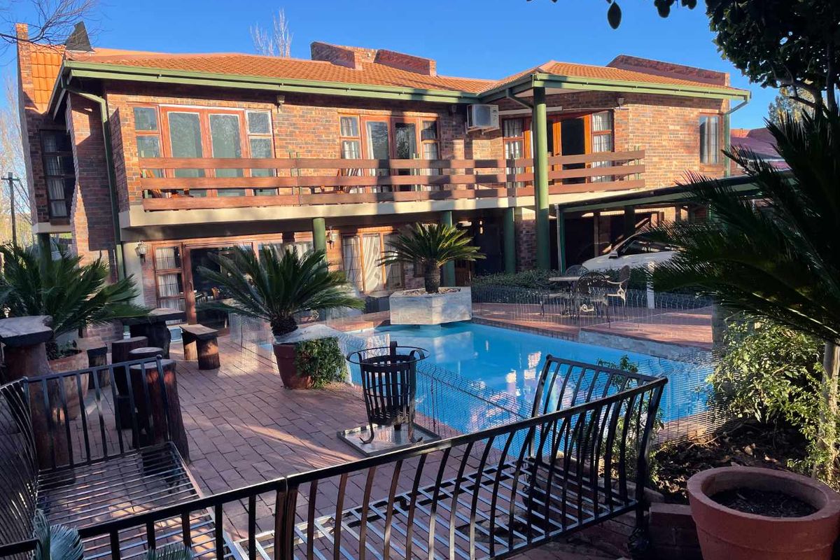 Rear view of a double-story brick house featuring a swimming pool, paved patio area, and a wooden balcony on the upper level.